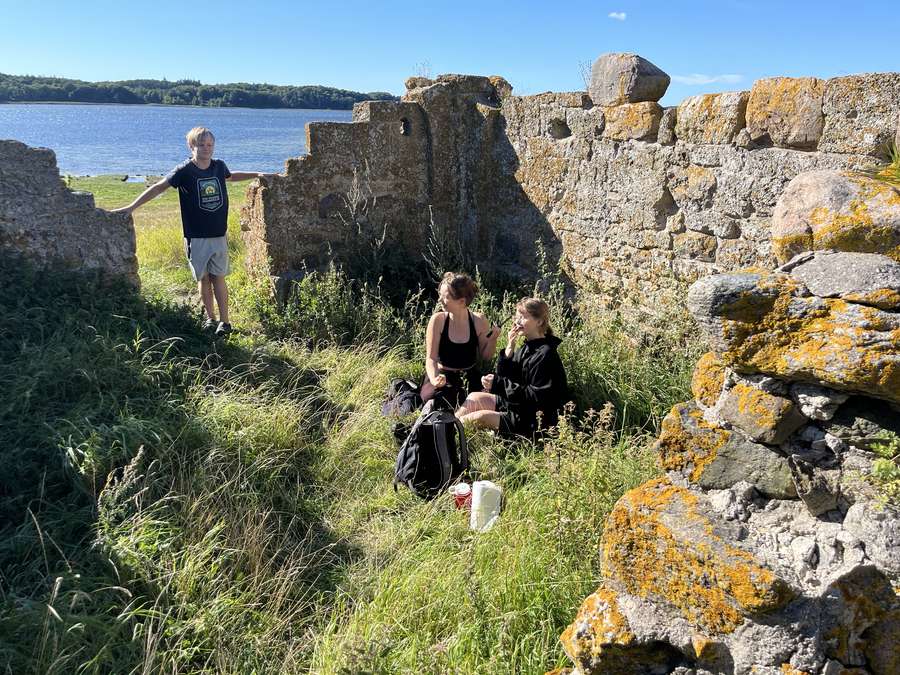Three teenagers among lichen-covered stone ruins by the water